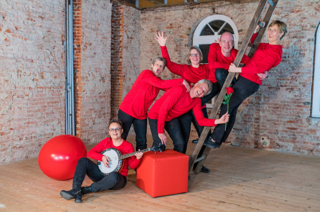 Foto Theatergruppe Platt up Zack in roter Kleidung possierend auf Leiter mit Banjo